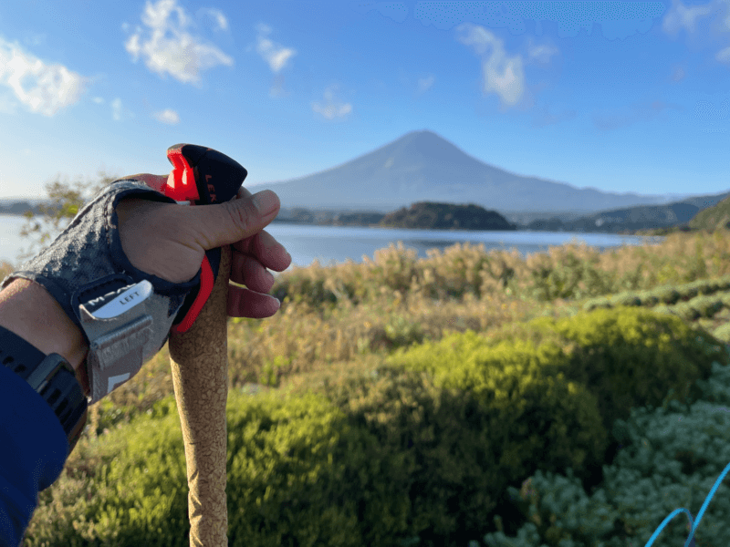ノルディックウォーキングのポールを握る筆者。河口湖の向こうに富士山が見える